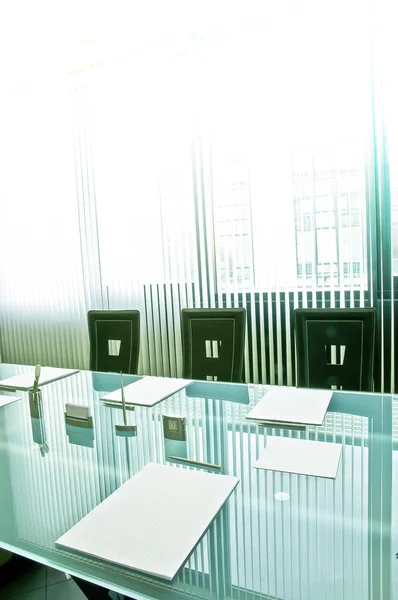 Waiting for the meeting. The crystal table set with paper pads for notes, pens and business cards reflects the curtains with vertical strips that cut the light of the large windows