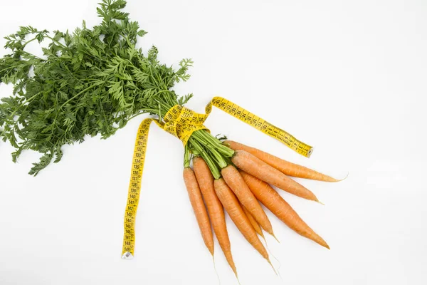 Vegetarian diet to reduce weight. A bunch of freshly picked carrots wrapped in a body measuring tape ruler which symbolizes the waistline