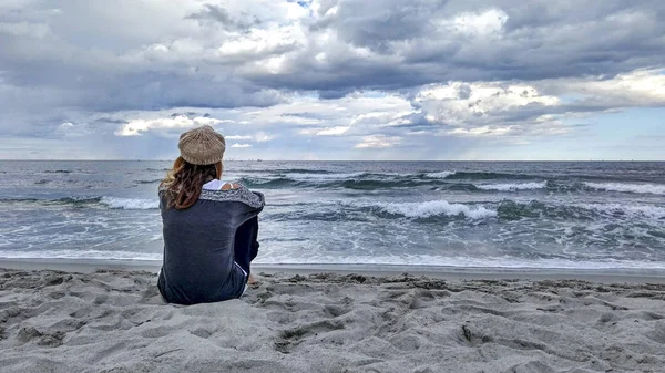 Young woman sitting by the sea with stormy sky, looks at the hor — Stock Photo, Image