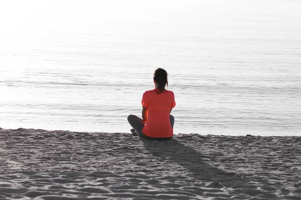 Young woman sitting on the shoreline of the sea at dawn in athle — Stock Photo, Image