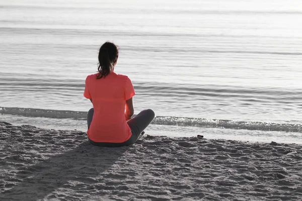 Young woman sitting on the shoreline of the sea at dawn in athle — Stock Photo, Image