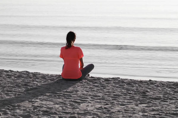 Young woman sitting on the shoreline of the sea at dawn in athle — Stock Photo, Image