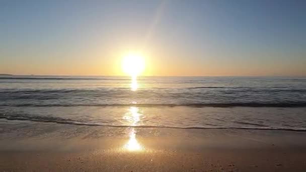 影片沿着靠近地面的海岸运动 在黎明时分在背光下冲上沙上 太阳在前景 — 图库视频影像