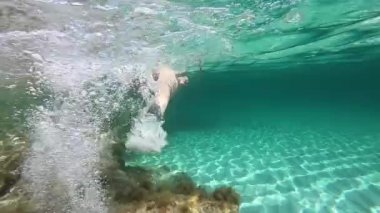 Suyun altından çekilen siyah bikinili güzel bir kadının yavaş çekimleri şeffaf sularda yüzerken kayalardan, renkli deniz bitkilerinden ve beyaz kumlardan oluşan deniz tabanında maske ve şnorkelle yüzmesi.