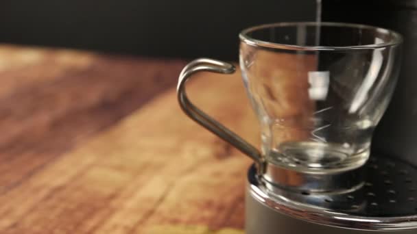 Vue d'angle de près du café expresso italien. La main d'une femme repose la tasse en verre sous les jets de la machine, le café remplit la tasse de fumée et de mousse et la femme la ramène 