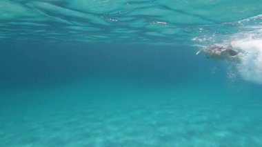 Alt kısmında etkileyici bir şeffaf mavi ve beyaz kum üzerinde maske ve şnorkel ile mavi suda sualtı yüzme tarafından çekilen siyah bir bikini güzel bir genç kadının yavaş hareket
