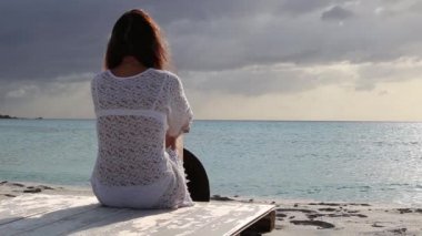 Deniz in arkasından oturan genç kadın, beyaz dantel bir elbise ve beyaz bir iç çamaşırı ve uzun saçlı, rüzgarda şafakta ufka bakar