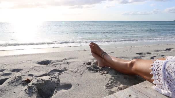 黎明时分 一位年轻女子坐在海边的风中 在平坦的海水上反射太阳的腿 — 图库视频影像