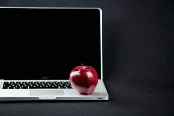 Manzana roja brillante descansando sobre un portátil de aluminio abierto en enfoque selectivo sobre un fondo negro —  Fotos de Stock