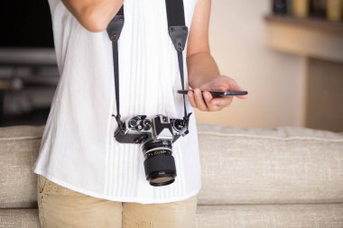 Eski ve modern zamanlar arasında kontrast: boynuna vintage kamera ile genç bir kadın akıllı telefon ile keman