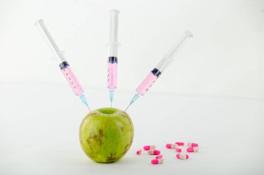 Kavram: doğanın insan Gdo manipülasyon ve göreceli zehirli meyve. Üç şırınga ile kirlenmiş bir elmanın yakın çekim ve beyaz arka plan daki ilaçlar