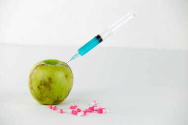 Kavram: doğanın insan Gdo manipülasyon ve göreceli zehirli meyve. Bir şırınga ile kontamine olmuş bir elmanın yakın çekim ve beyaz arka plan daki ilaçlar