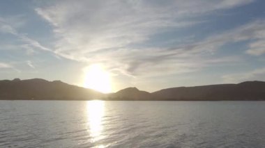 Arka planda dağ silueti olan gölün üzerinde dramatik bir gün batımı manzarası ve arka planda bir kuş, düz bir profil içinde güneşin üzerinden geçiyor.