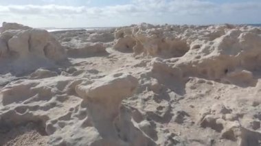 Kireçtaşı kayalarının düşük açılı görüntüsü, yabancı bir gezegende alçaktan uçan bir uçuşa benzer. Arka planda güneşin yansıması vardır. Suyun arka planında ve bulutlu gökyüzünde düz bir profil oluşturur.