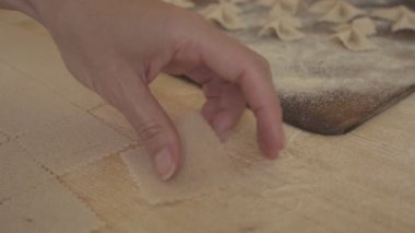 Yavaş çekimde ev yapımı vejetaryen farfalle makarna ile buğday unu arasındaki süreci yakından incele. Aşçı hamuru odun kesme tahtasında yoğurur, geleneksel İtalyan makarnası.