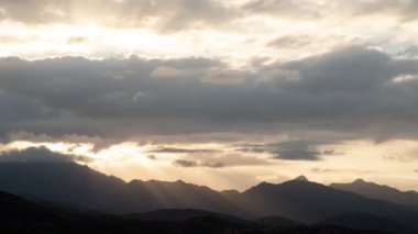 4k dramatik bulutlu gün batımı zamanı gökyüzü - Güneş ışınları dağların arkasına geçmeden önce kara bulutların içine sızar