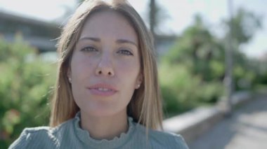 Genç ve güzel bir kadın kameraya ciddi ciddi bakıyor sonra gülümsüyor ve yüz koruma maskesi takıyor.