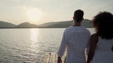 Karışık ırk aşıkları çifti, İspanyol ve Kafkasyalı, eski ahşap bir iskelede yürüyüp gün batımına ya da şafağa bakıyorlar. 