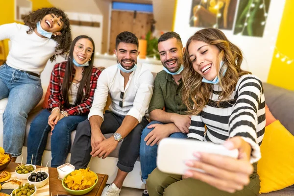 Bir grup melez arkadaş evde tıbbi koruma maskesiyle selfie çekiyorlar Coronavirus 'un yeni normallik saatinde evde mutlu insanlar için aperatif partisi.