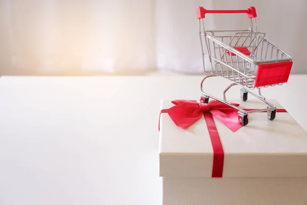 Close-up of gift boxes and shopping cart  on white desk