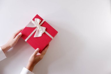 Yakın çekim kadın gönderen kırmızı hediye kutusu beyaz arka plan üzerinde beyaz kurdele ile eller