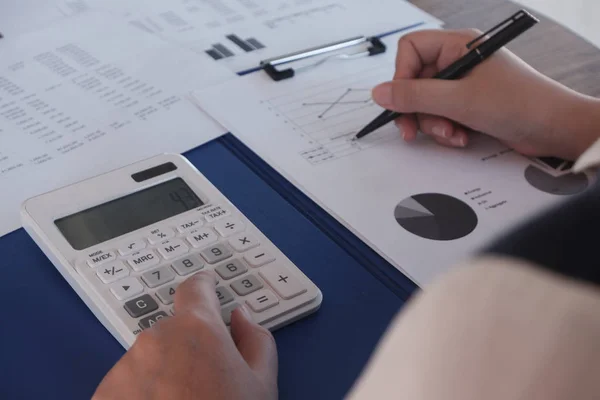 Female working in office, studying using calculator and writing something with documents and chart on table