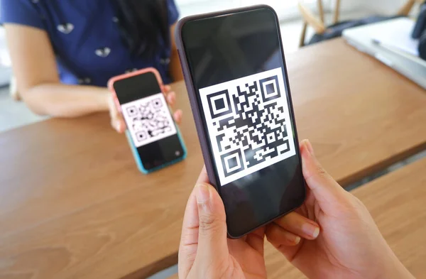 Women's hand uses a mobile phone application to scan QR codes in stores that accept digital payments without money and plastic tags on the table. QR code payment and cashless technology concept .