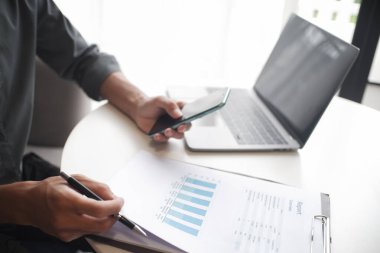 İş yerinde cep telefonu ve dizüstü bilgisayar kullanan işadamının eli.