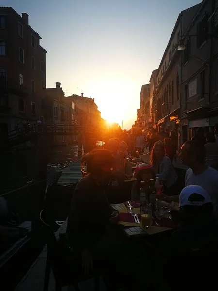 Uteserveringar och folk som ter i Venedig i kvllssolen. 