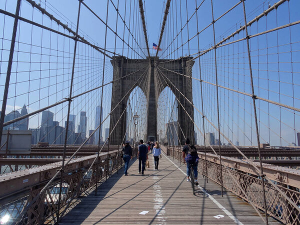 Brooklyn, New York, USA - 31st May 2017 : View of the famous Brooklyn Bridge pylon, the skyline of Manhattan and people walking on the bridge