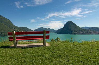 Lugano Gölü 'nün (Ceresio Gölü) güzel panoramik manzarası, kırmızı bir bank ve arka planda Monte San Salvatore Lugano, Ticino, İsviçre' deki Parco San Michele 'den görülüyor.