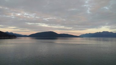 Pasifik Okyanusu 'nda dağ dolu ufukta. Bulutlar kapalı parlayan parlak renkler ile gün batımı içinde geçiş Alaska içinde