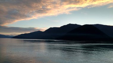 Pasifik Okyanusu 'nda dağ dolu ufukta. Bulutlar kapalı parlayan parlak renkler ile gün batımı içinde geçiş Alaska içinde