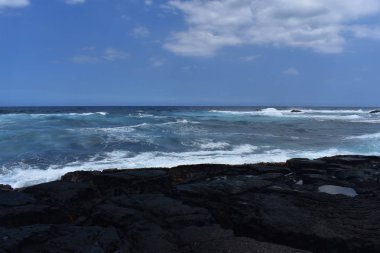 Dalgalar mavi bir gökyüzü altında kayalar üzerinde yıkamak gibi Hawaii beyaz köpük Rocky Shore üzerinde çökmesini dalgalar