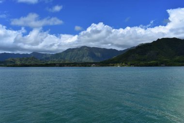 Mavi gökyüzünün altında bulutlarla Okyanustan Dağların Görünümü