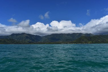 Mavi gökyüzünün altında bulutlarla Okyanustan Dağların Görünümü