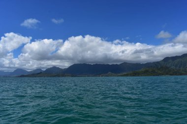 Mavi gökyüzünün altında bulutlarla Okyanustan Dağların Görünümü