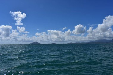 Mavi gökyüzünün altında bulutlarla Okyanustan Dağların Görünümü