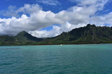 Mavi gökyüzünün altında bulutlarla Okyanustan Dağların Görünümü