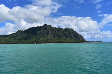Mavi gökyüzünün altında bulutlarla Okyanustan Dağların Görünümü