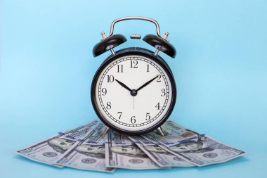 Çalar saat mavi bir arka plan üzerinde para yığını üzerinde duruyor