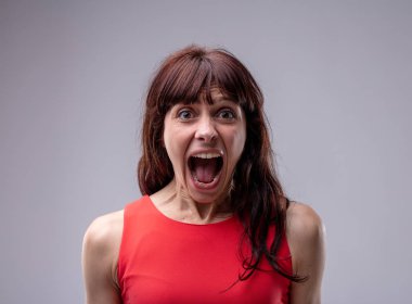 Excited exuberant woman standing screaming at the camera with her mouth wide open isolated on grey clipart