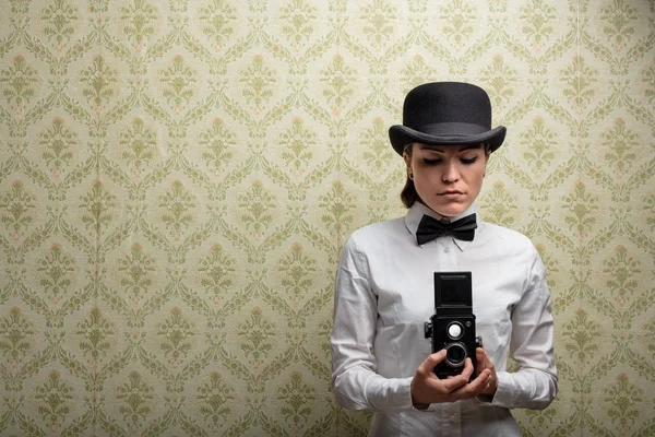 Elegant Årgangskvinnefotograf Med Bowlerhatt Sløyfe Som Holder Gammelt Kamera Mot – stockfoto