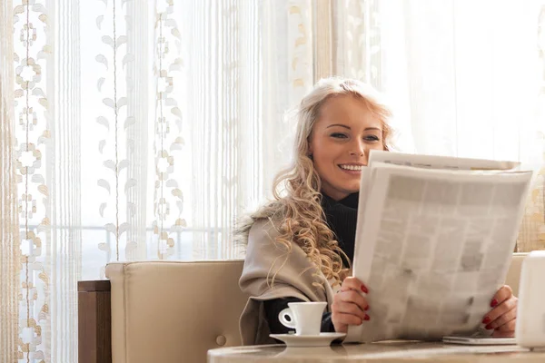 Mujer joven sonriendo mientras lee el periódico matutino — Foto de Stock