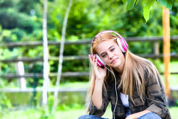 Mujer joven rubia listando música en auriculares — Foto de Stock