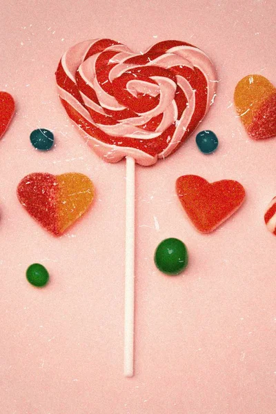 Lollipop in the shape of heart and candies on pink background