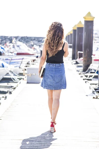Young woman walking on pier of boats with book in hand