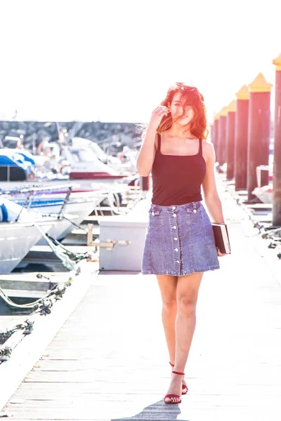 Young woman walking on pier of boats with book in hand