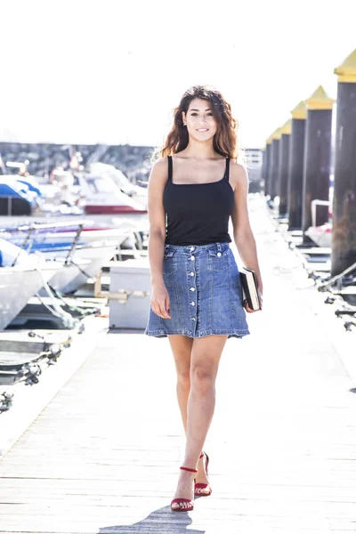 Young woman walking on pier of boats with book in hand