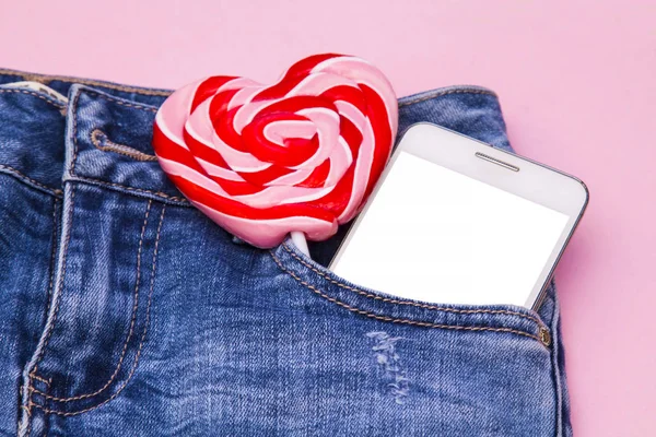 heart lollipop and mobile phone in the blue jean pocket